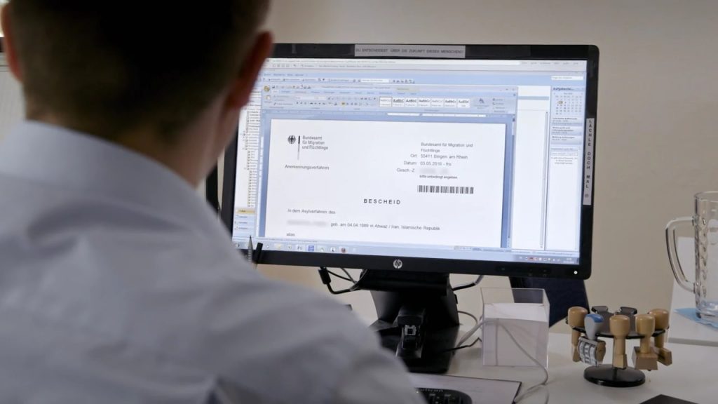 Du Entscheidest über die Zukunft dieses Menschen. BAMF-Mitarbeiter am Computer. (c) HANFGARN & UFER Filmproduktion